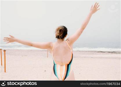 Young woman in a swimsuit back, jumping and celebrating during a sunny day at the beach, liberty and holiday concept, copy space