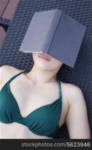 Young woman in a swimsuit lying down and relaxing with a book over her face