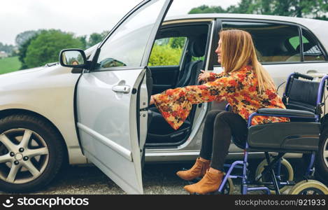 Young woman in a wheelchair getting on the car. Woman in wheelchair getting on car