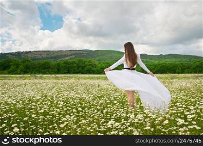Young woman in a white dress in a field of chamomile flowers