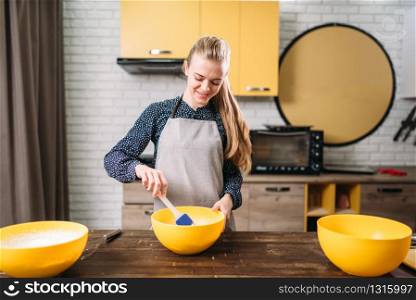 Young woman in apron stir the dough in a bowl on wooden table. Sweet cake cooking preparation