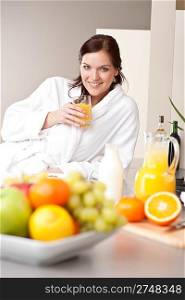 Young woman in bathrobe drink orange juice for breakfast in kitchen