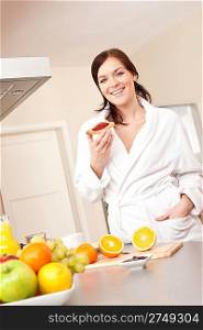 Young woman in bathrobe eating toast for breakfast in kitchen