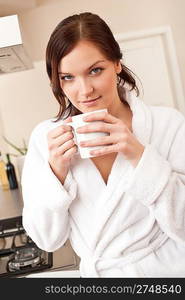 Young woman in bathrobe enjoying cup of coffee in kitchen