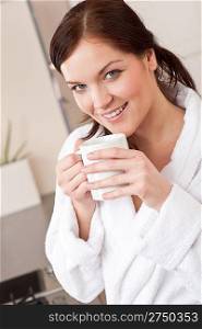 Young woman in bathrobe enjoying cup of coffee in kitchen