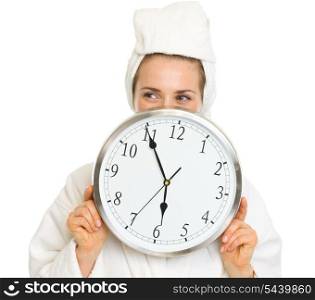 Young woman in bathrobe hiding behind clock