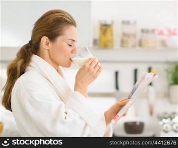 Young woman in bathrobe with magazine and drinking milk