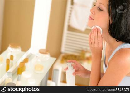 Young woman in bathroom clean face make-up removal looking mirror
