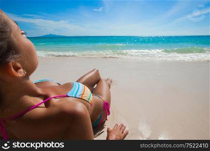 Young woman in bikini laying at seaside, rear view. Woman laying at seaside