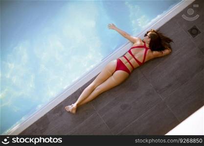 Young woman in bikini posing by the swimming pool outdoor at summer day