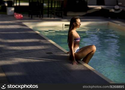 Young woman in bikini posing by the swimming pool outdoor at summer day