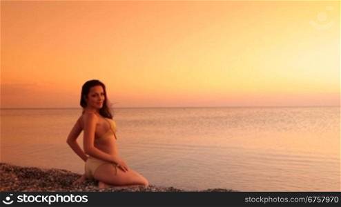 Young Woman in bikini sitting on beach at sunset