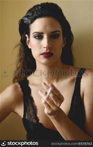 Young woman in black lingerie smoking cigarette. Young beautiful brunette woman smoking cigarette on yellow background. Girl wearing black lingerie.