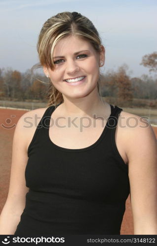 Young woman in black tank top outside at jogging track. Great smile, beautiful teeth.