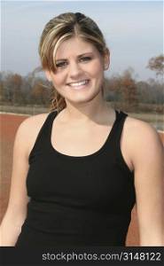 Young woman in black tank top outside at jogging track. Great smile, beautiful teeth.