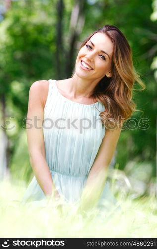 young woman in blue dress sitting on grass. beautiful young woman in blue dress sitting on grass