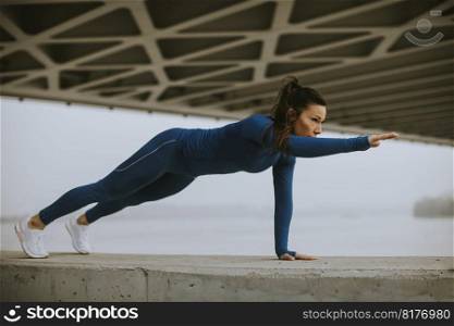 Young woman in blue track suit doing pushups under the bridge in the urban environment