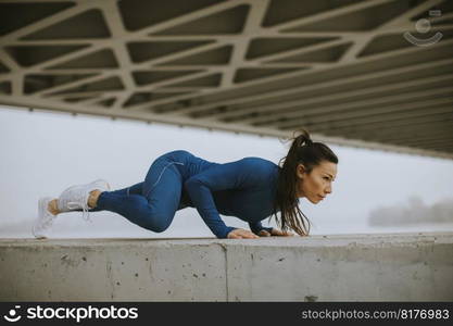 Young woman in blue track suit doing pushups under the bridge in the urban environment