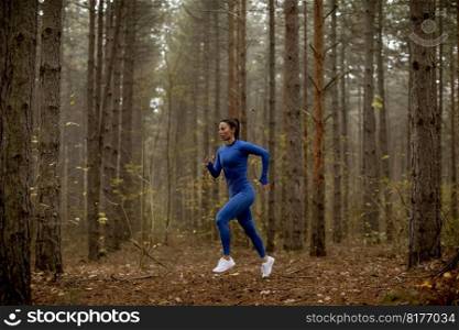 Young woman in blue track suit running on the forest trail at autumn