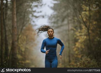 Young woman in blue track suit running toward camera on the forest trail at autumn