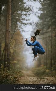 Young woman in blue track suit taking high jump on the forest trail at autumn