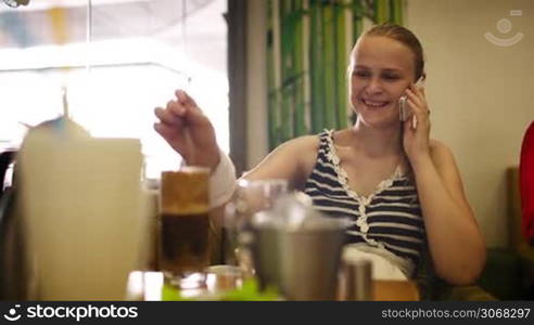 Young woman in cafe speaking on the phone and drinking cocktail through a straw.