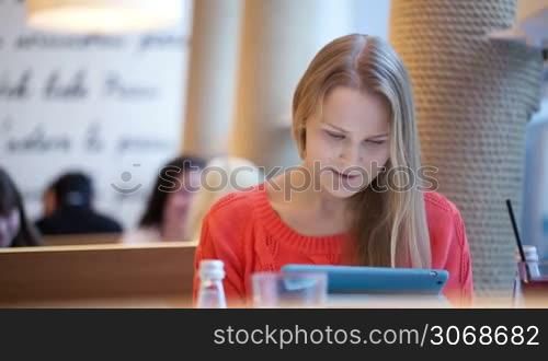 Young woman in cafe using her touchpad, defocused people in the background