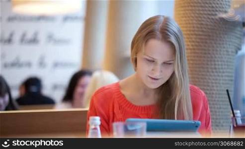 Young woman in cafe using her touchpad, defocused people in the background