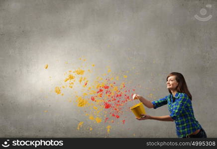 Young woman in casual holding yellow bucket with splashes. Add some color