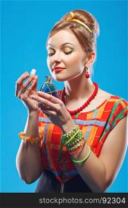 Young woman in colorful old-fashion clothes in pin up style holding an opened bottle of perfume and smelling it