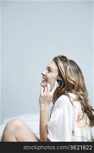 Young woman in dressing gown, using mobile phone in bedroom