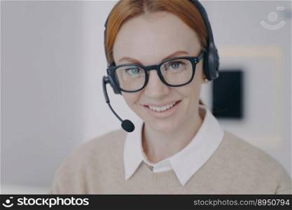 Young woman in earphones sitting at workplace. Online consultant of call center. Caucasian friendly girl in headset provides information by telephone. Customer support concept.. Online consultant of call center. Young woman in earphones provides information by telephone.