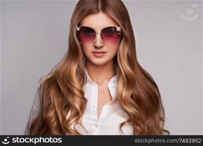 Young woman in elegant sunglasses. Blond hair, isolated studio shot. Fashion lookbook. Brunette girl with long healthy and shiny curly hair