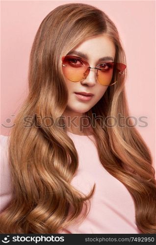 Young woman in elegant sunglasses. Blond hair, pink dress, isolated studio shot. Fashion lookbook. Brunette girl with long healthy and shiny curly hair