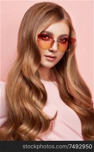 Young woman in elegant sunglasses. Blond hair, pink dress, isolated studio shot. Fashion lookbook. Brunette girl with long healthy and shiny curly hair