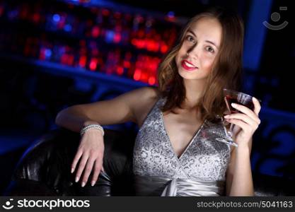 Young woman in evening dress in night club with a drink