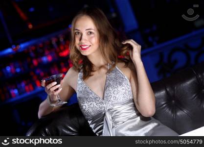 Young woman in evening dress in night club with a drink