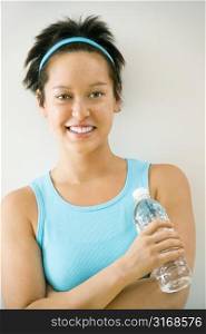 Young woman in exercise clothes holding bottle of water smiling.