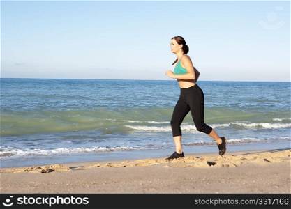 Young Woman In Fitness Clothing Running Along Beach