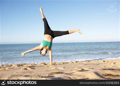 Young Woman In Fitness Clothing Turning Cartwheel On Beach