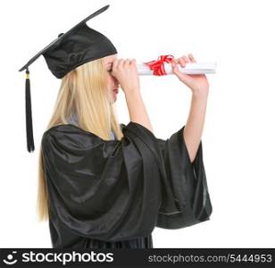 Young woman in graduation gown looking into distance through diploma