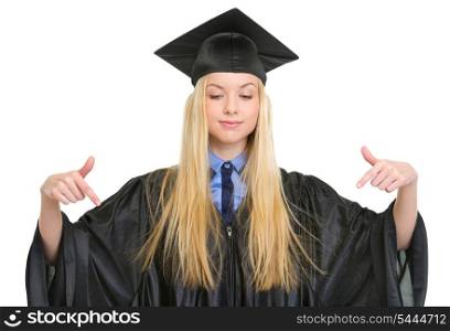 Young woman in graduation gown pointing down on copy space