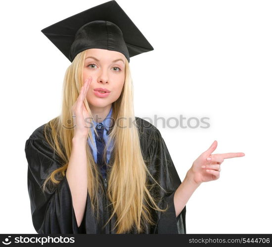 Young woman in graduation gown pointing on copy space