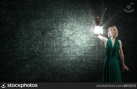 Young woman in green dress with lantern in darkness. Bright ideas