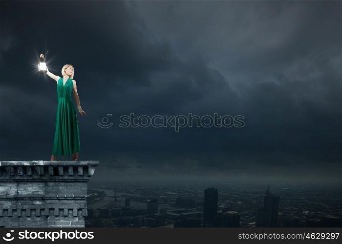 Young woman in green dress with lantern in darkness. Lost in darkness