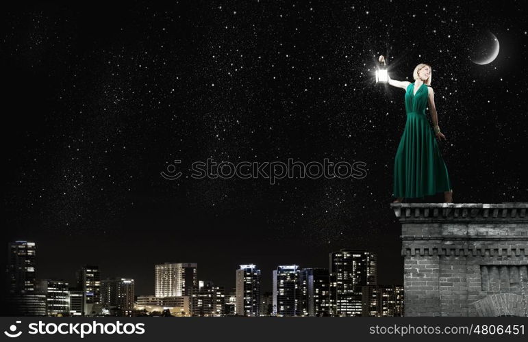 Young woman in green dress with lantern in darkness. Lost in darkness