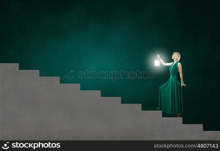 Young woman in green dress with lantern in darkness. Lost in darkness