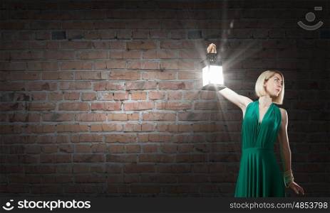Young woman in green dress with lantern in darkness. Lost in darkness