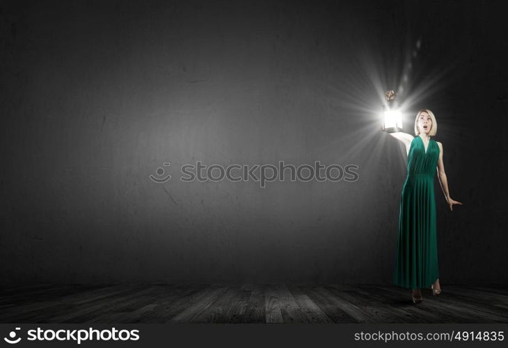 Young woman in green dress with lantern in darkness. Lost in darkness