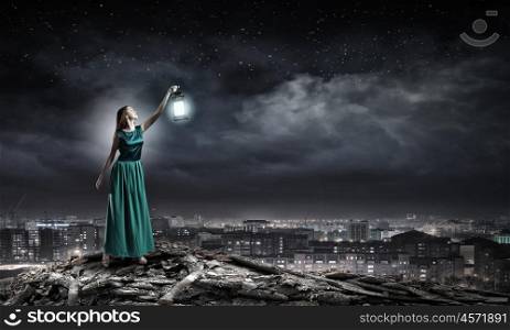Young woman in green dress with lantern walking in darkness. Lost in darkness